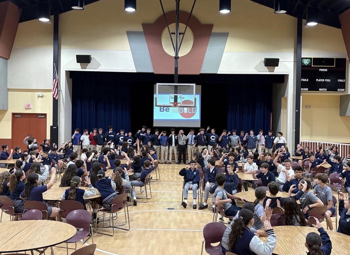 B.O.L.D. student presentation in the school gymnasium with the Be B.O.L.D. slide on screen